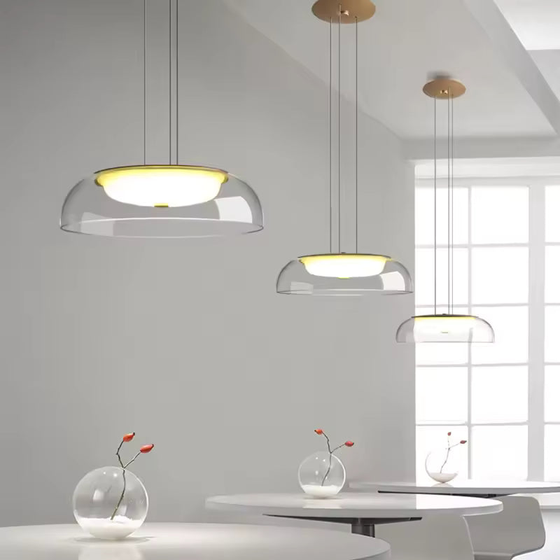 Dans un intérieur épuré, trois suspensions en verre transparent à diffuseur opalin affichent un design moderne et aérien