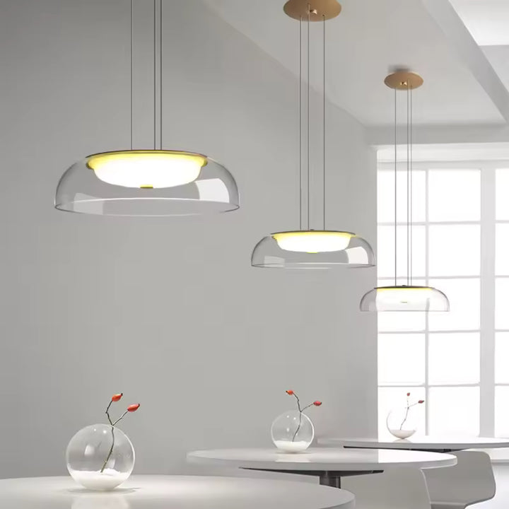 Dans un intérieur épuré, trois suspensions en verre transparent à diffuseur opalin affichent un design moderne et aérien