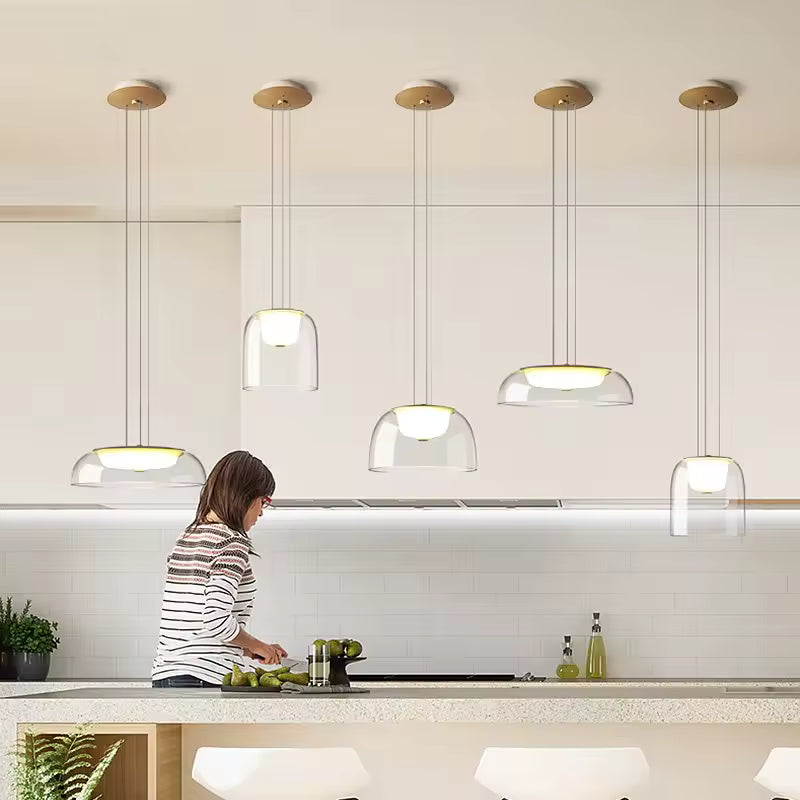 Plusieurs suspensions en verre transparent à diffuseur opalin éclairent une cuisine contemporaine au style épuré