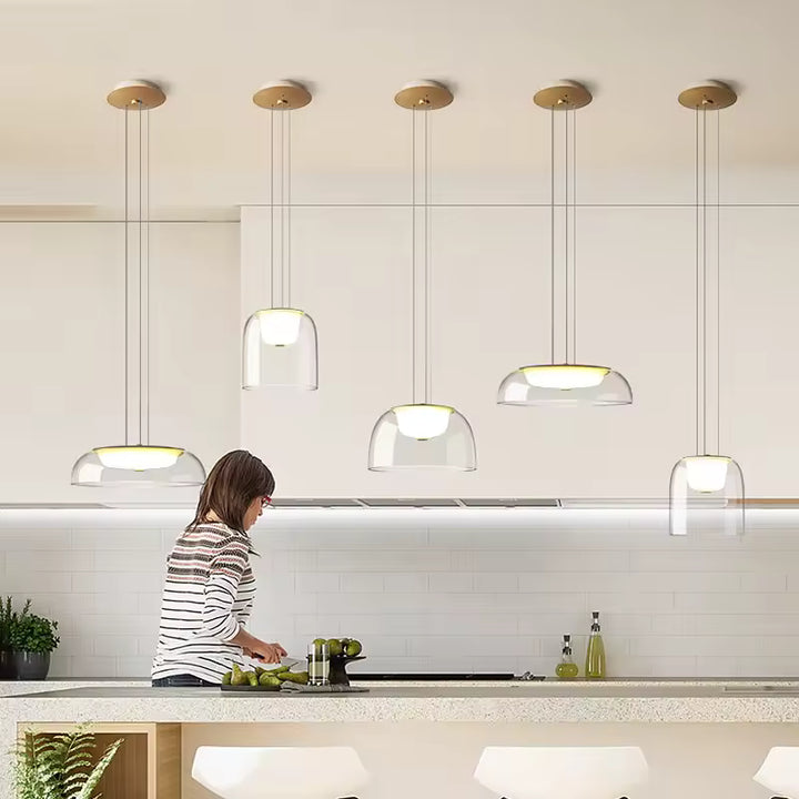 Plusieurs suspensions en verre transparent à diffuseur opalin éclairent une cuisine contemporaine au style épuré