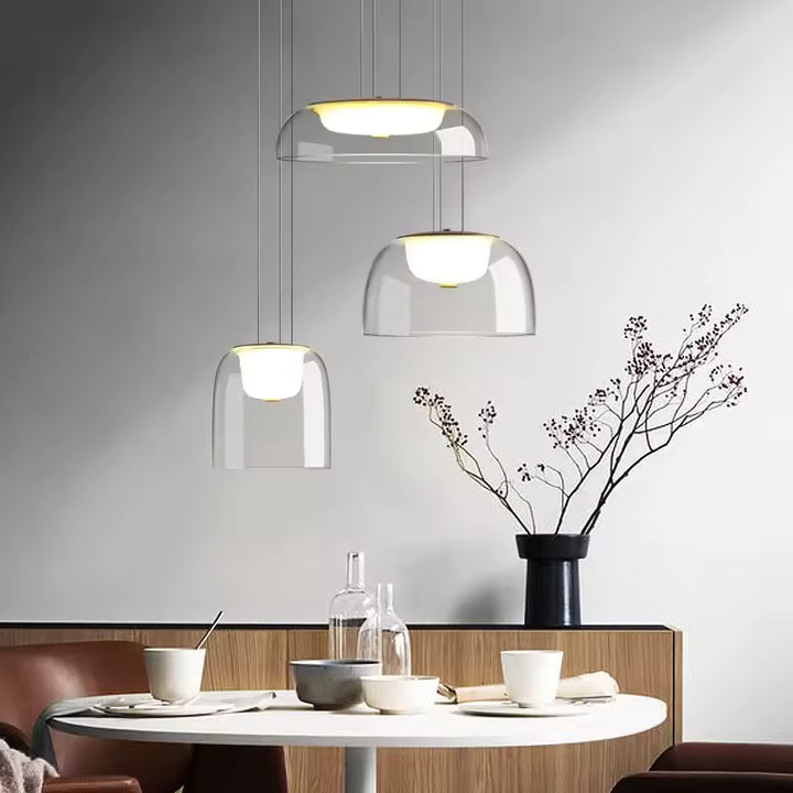 Au-dessus d’une table, trois suspensions en verre transparent à diffuseur opalin créent une ambiance japandi épurée