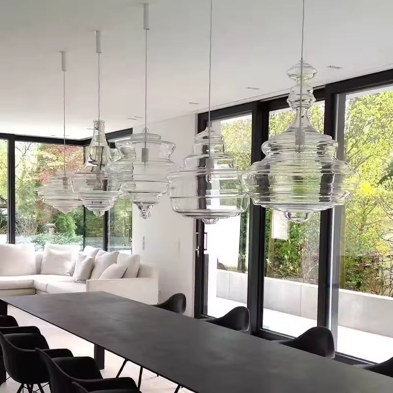Alignement de suspensions en verre transparent aux formes sculpturales étagées, au-dessus d'une grande table contemporaine.