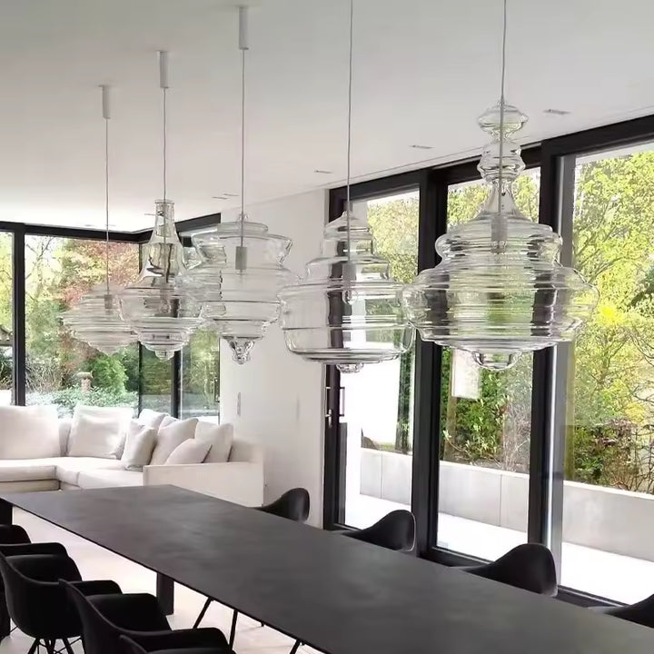 Alignement de suspensions en verre transparent aux formes sculpturales étagées, au-dessus d'une grande table contemporaine.
