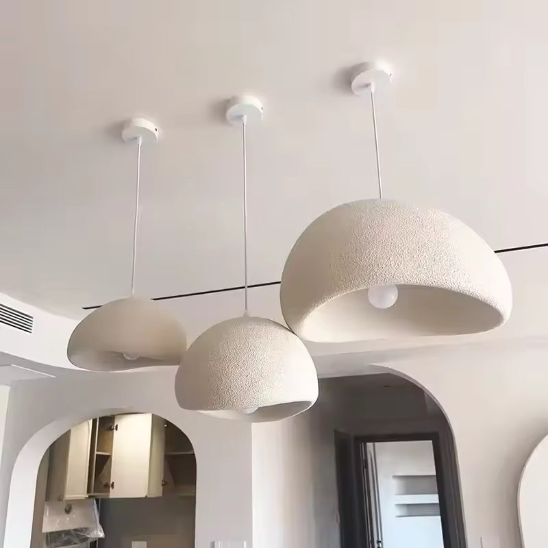 Trois suspensions wabi-sabi blanches aux dômes asymétriques et texturés, dans un intérieur moderne aux arches arrondies.