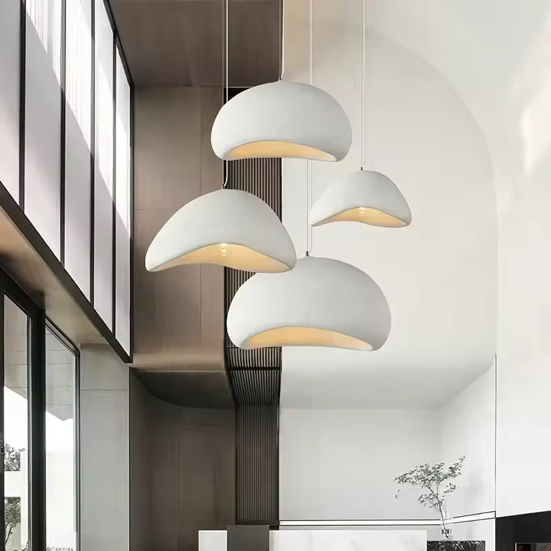 Quatre suspensions blanches aux dômes asymétriques habillent un plafond haut dans une entrée contemporaine au design épuré.
