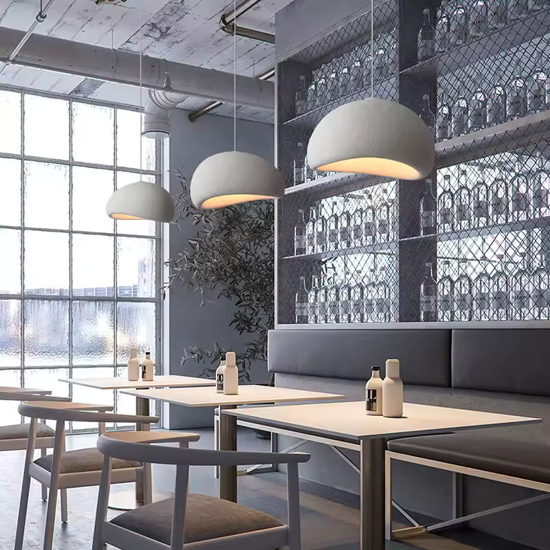 Dans un restaurant au décor industriel, trois suspensions blanches à dôme organique éclairent les tables avec douceur.