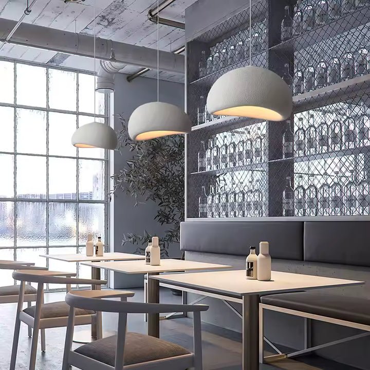 Dans un restaurant au décor industriel, trois suspensions blanches à dôme organique éclairent les tables avec douceur.