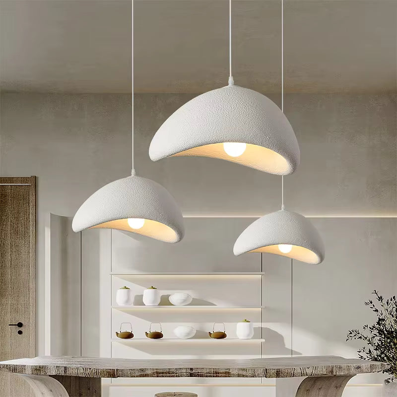 Au-dessus d'une table en bois brut, trois suspensions blanches asymétriques au relief minéral créent une ambiance naturelle et Japandi.