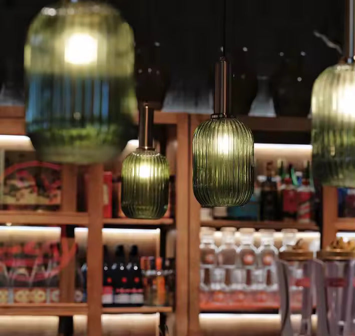 Suspensions en verre cannelé vert avec finitions dorées éclairant un bar ou un restaurant. Ces luminaires décoratifs créent une ambiance chaleureuse et raffinée, idéale pour les espaces de restauration modernes.