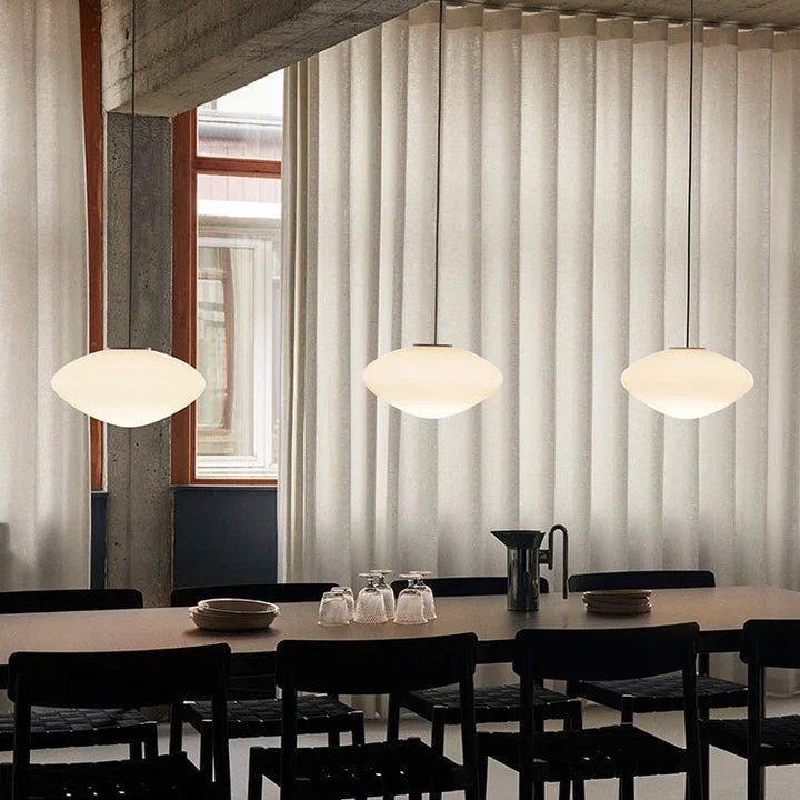 Trio de lampes suspendues en verre opalin alignées au-dessus d'une grande table de salle à manger.