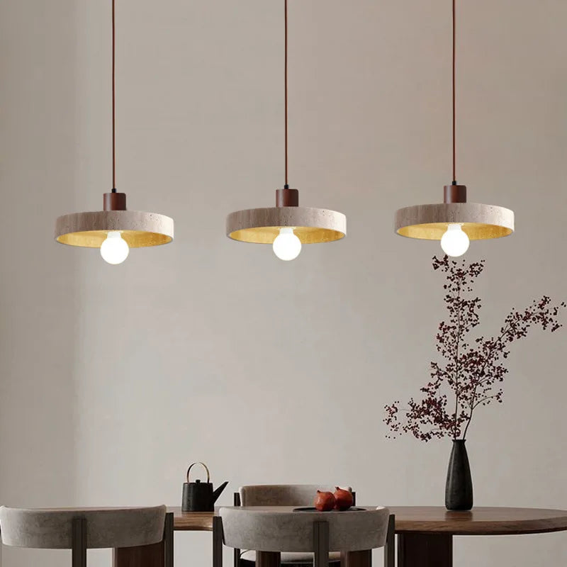 Alignement de trois suspensions disque en travertin et bois foncé au-dessus d'une longue table de salle à manger.
