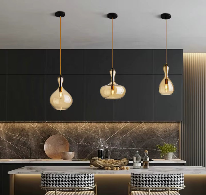 Trois suspensions en verre ambré aux formes fluides, sublimant un îlot de cuisine moderne aux finitions noires et marbrées.