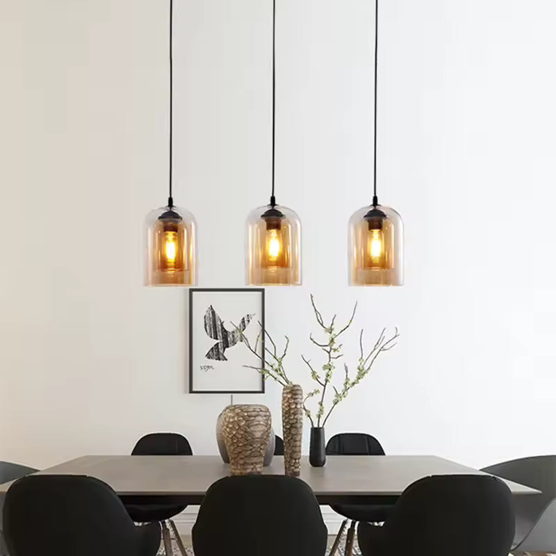 Trois suspensions en verre ambré diffusent une lumière chaude au-dessus d'une table à manger au style scandinave épuré.