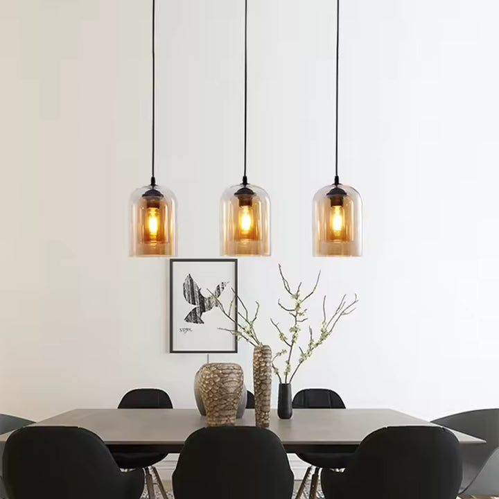 Trois suspensions en verre ambré diffusent une lumière chaude au-dessus d'une table à manger au style scandinave épuré.