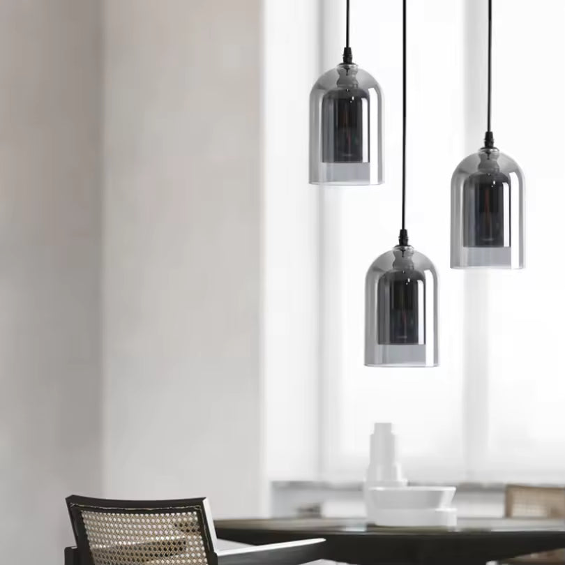 Composition de trois suspensions en verre fumé à hauteurs décalées, au design géométrique et minimaliste, au-dessus d'une table.
