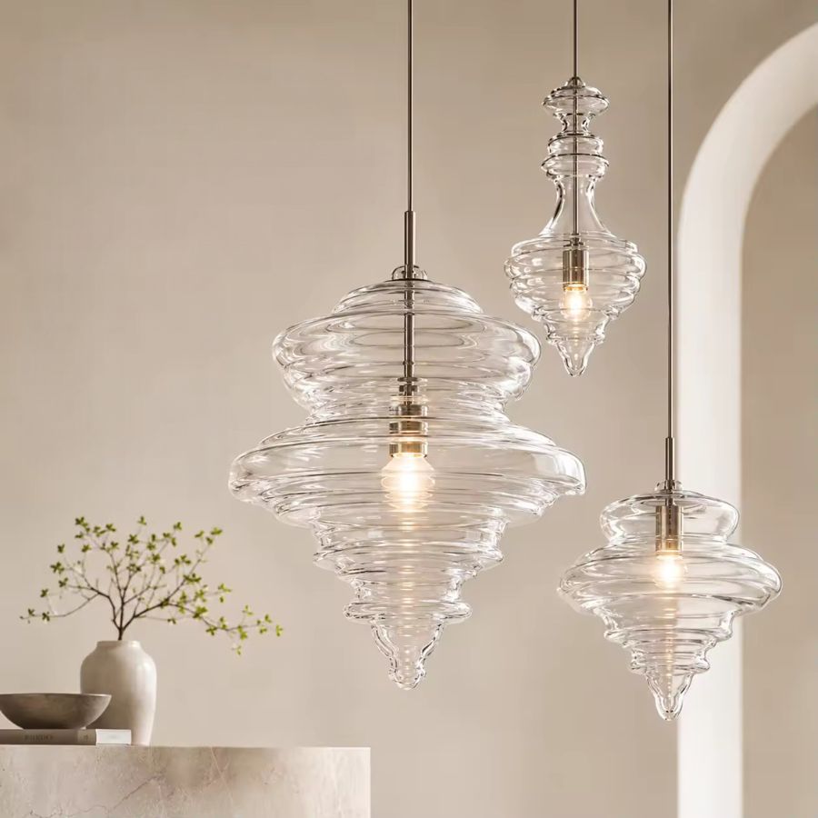 Trois suspensions en verre transparent aux reliefs ondulés et formes élancées, dans un intérieur contemporain raffiné.