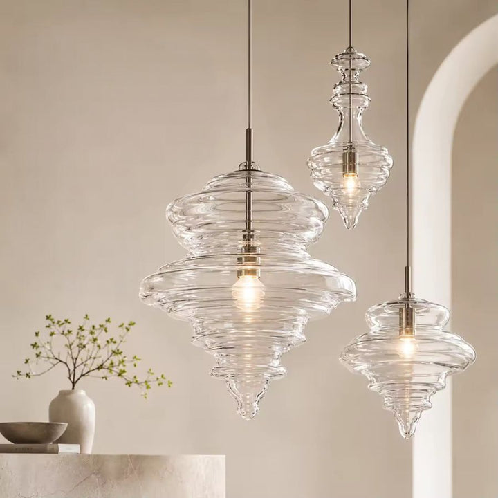 Trois suspensions en verre transparent aux reliefs ondulés et formes élancées, dans un intérieur contemporain raffiné.