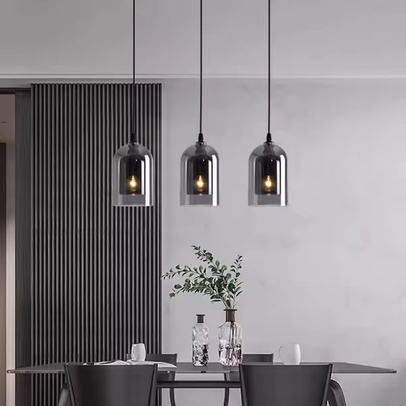 Trois suspensions en verre fumé alignées au-dessus d'une table à manger, pour une ambiance moderne et élégante aux accents industriels.