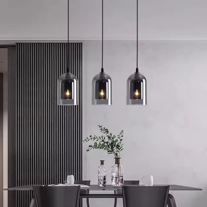 Trois suspensions en verre fumé alignées au-dessus d'une table à manger, pour une ambiance moderne et élégante aux accents industriels.