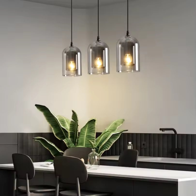 Alignement de trois suspensions en verre fumé aux formes arrondies, éclairant un îlot de cuisine moderne aux accents industriels.