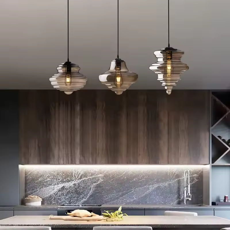 Trio de suspensions en verre fumé aux silhouettes sculpturales étagées, au-dessus d'un îlot de cuisine contemporain.