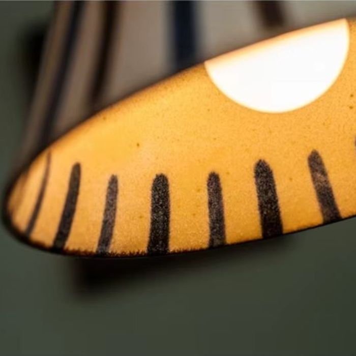 Zoom sur la suspension céramique écrue avec motifs géométriques bleus et bruns, créant une ambiance vintage chic dans votre salon ou cuisine.